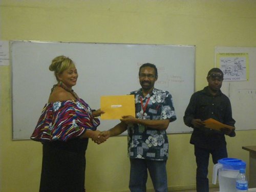 Fijian National Selaima Smith receives her sewing certificate from POM Branch Manager Mr. Bernard Paru. Looking on is the Adult Literacy Program Manager Mr Aquino Saklo. 